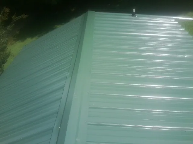 New green metal panels meeting at the ridge of a roof — Flat Roof Repair work by our crew in Ferris