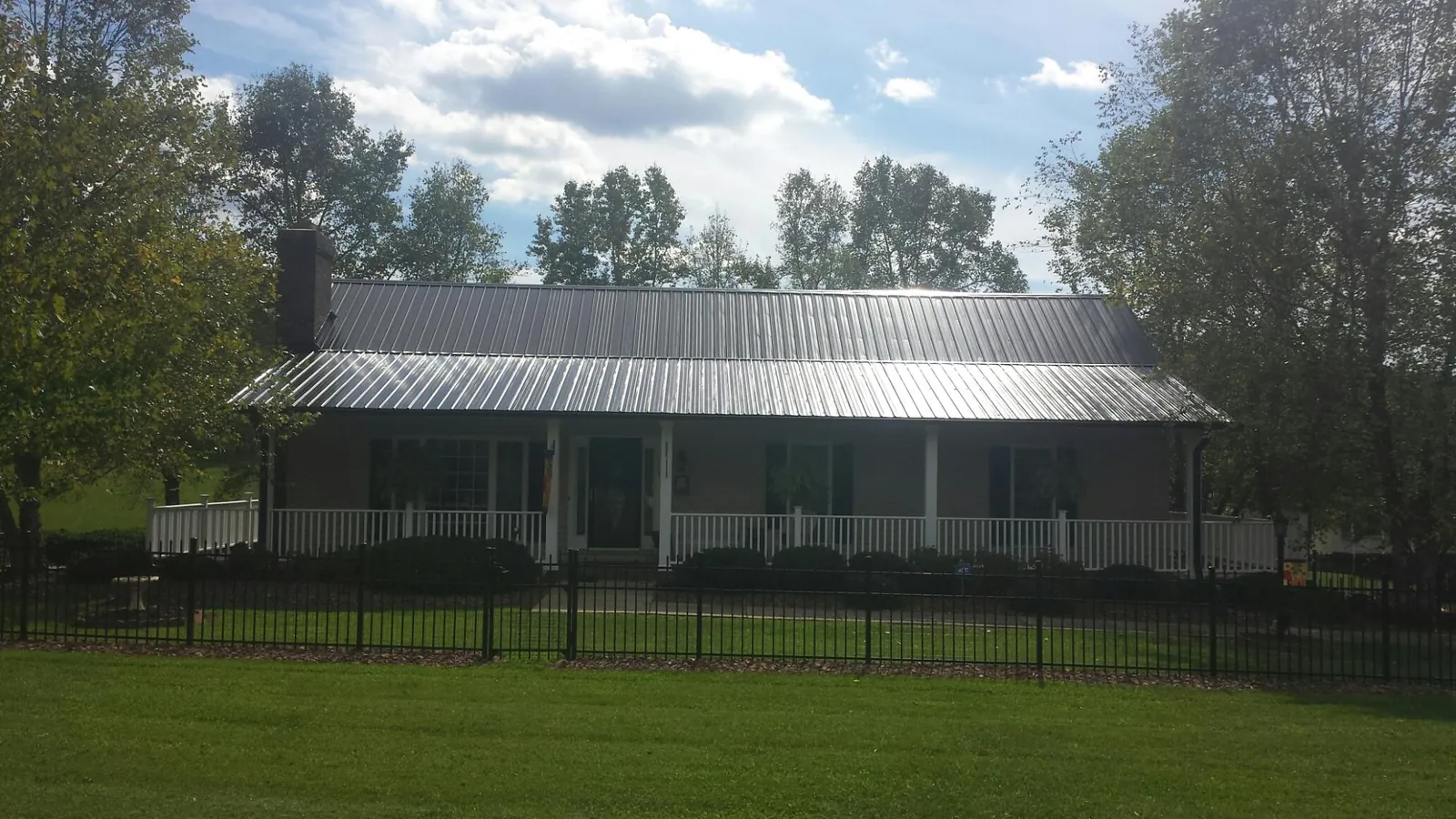Gray metal roof on a brick ranch with a full width front porch — Gutter Guard Installation work by our crew in Ferris