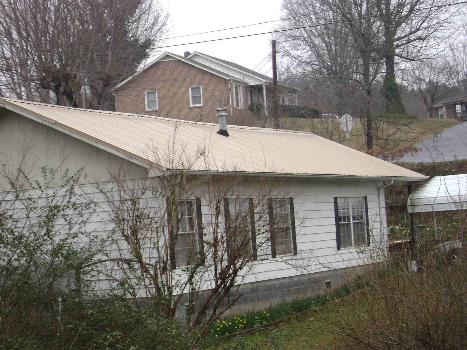 Tan metal roof on a white sided house set into a hillside — Commercial Roofing by Roofing Brothers in Ferris