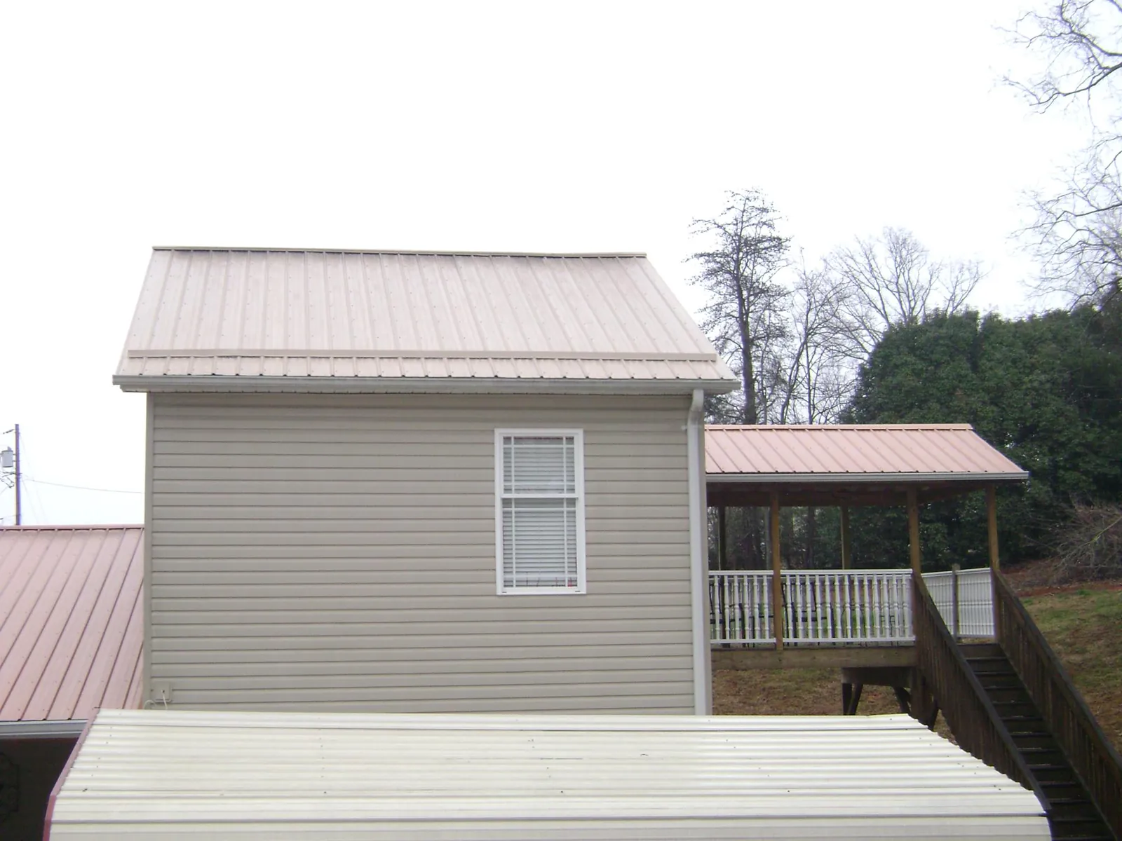 Tan metal roofs on a two story addition and attached porch, from a Roof Replacement job in Ferris